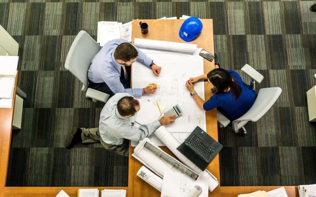 Overhead view of a team reviewing building plans with blueprints, a hard hat and a calculator